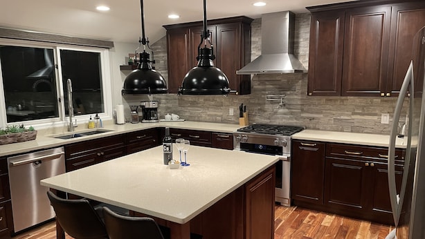 A modern kitchen with dark wood cabinets, a large island with bar stools, stainless steel appliances, and pendant lighting. - Willow Creek Oasis with Amazing Outdoor Kitchen (Centennial)