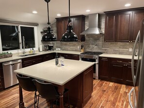 A modern kitchen with dark wood cabinets, a large island with bar stools, stainless steel appliances, and pendant lighting.