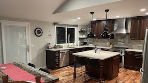 A modern kitchen with wooden flooring, a central island, dark cabinets, and pendant lighting. - Willow Creek Oasis with Amazing Outdoor Kitchen (Centennial)