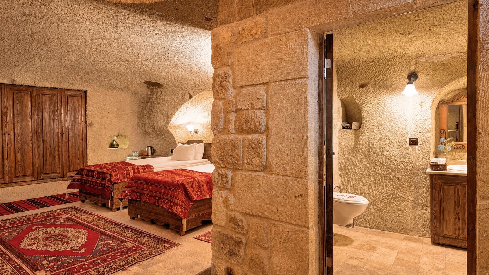 A room with a bed, a wooden wardrobe, a stone wall, and a bathroom with a toilet.