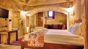 Una habitación con pared de piedra, cama de madera, televisión y ventana con vistas.