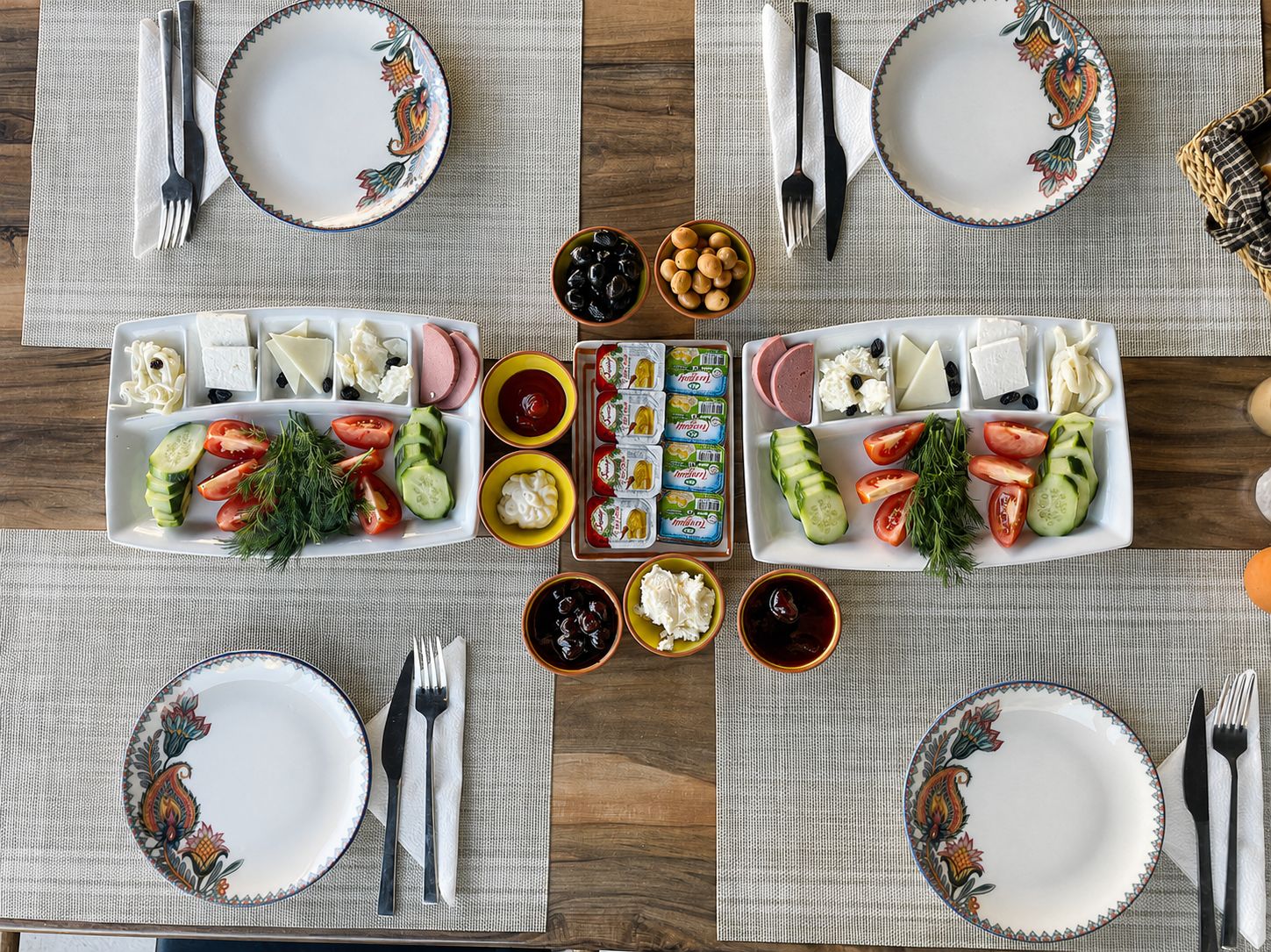 Una mesa lista para comer, con platos, cubiertos y diversos alimentos como queso, aceitunas y verduras.