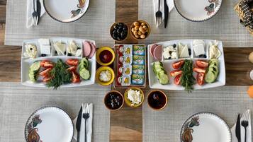 Una mesa lista para comer, con platos, cubiertos y diversos alimentos como queso, aceitunas y verduras.
