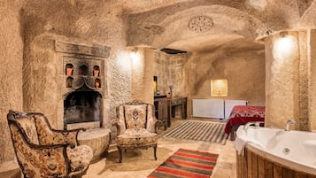 A room with a stone fireplace, two armchairs, a wooden cabinet, a red rug, and a bathtub.