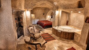 A stone-walled bathroom with a bathtub, a wooden chair, and a patterned rug. - Shiraz Cave Cappadocia (Ürgüp)