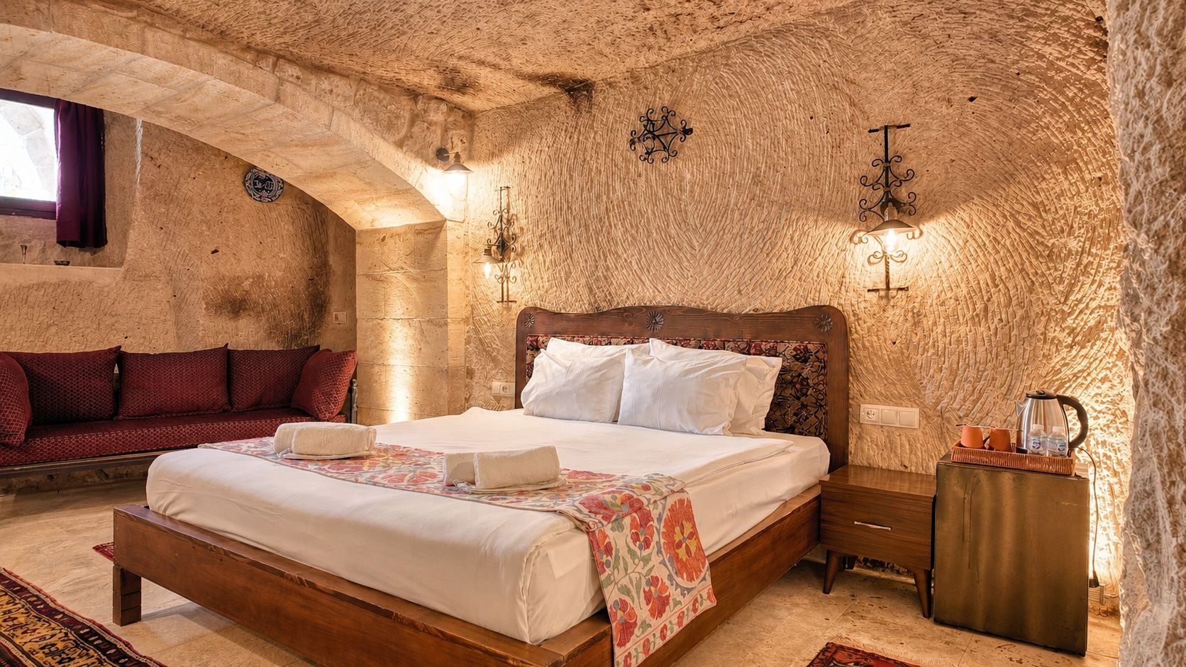 Un dormitorio con pared de piedra, una cama de madera, una mesita de noche y una ventana con cortinas.