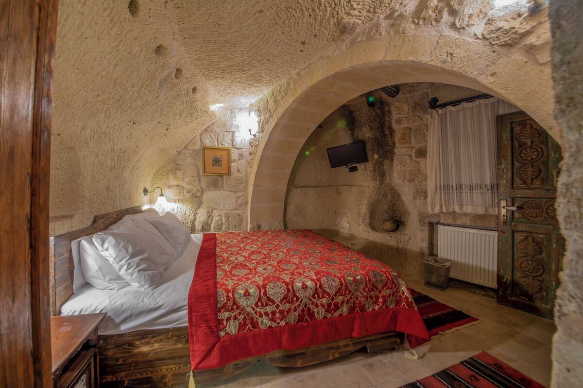 Um quarto aconchegante com cama, cabeceira de madeira, paredes de pedra, televisão e porta decorativa.