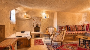 A cozy interior with a stone fireplace, a sofa with colorful cushions, and a wooden cabinet. - Shiraz Cave Cappadocia (Ürgüp)