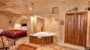 A room with a stone ceiling, a wooden bathtub, a bed with a red bedspread, and a wooden wardrobe. - Shiraz Cave Cappadocia (Ürgüp)