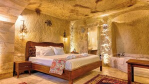 Een landelijke slaapkamer met een stenen muur, een houten bed, een nachtkastje, een bijzettafeltje, een badkamer met een bad en een houten bankje.