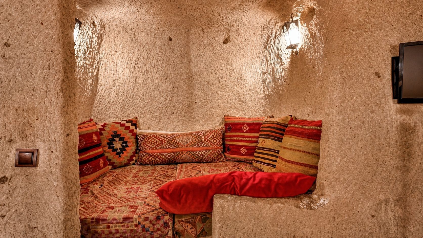 A cozy room with a textured wall, a sofa with patterned cushions, and a wall-mounted light fixture.