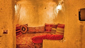 A cozy, stone-walled room with a cushioned seating area featuring patterned cushions. - Shiraz Cave Cappadocia (Ürgüp)