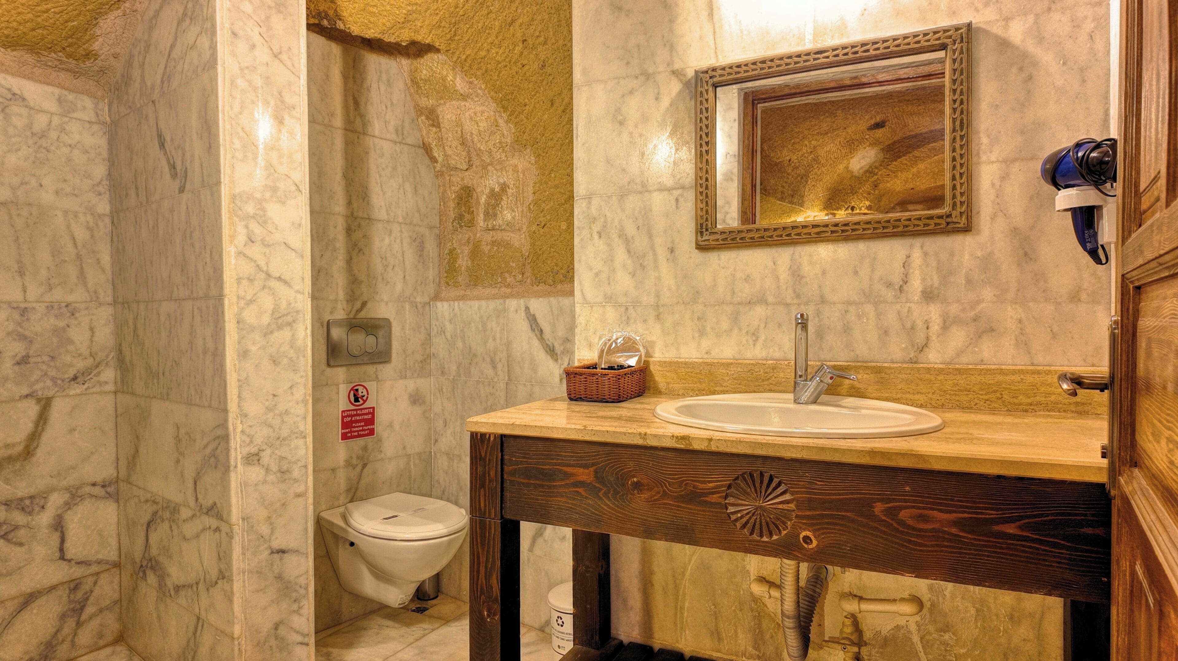 A bathroom with a marble floor, a wooden vanity with a sink and mirror, a toilet, and a shower area.