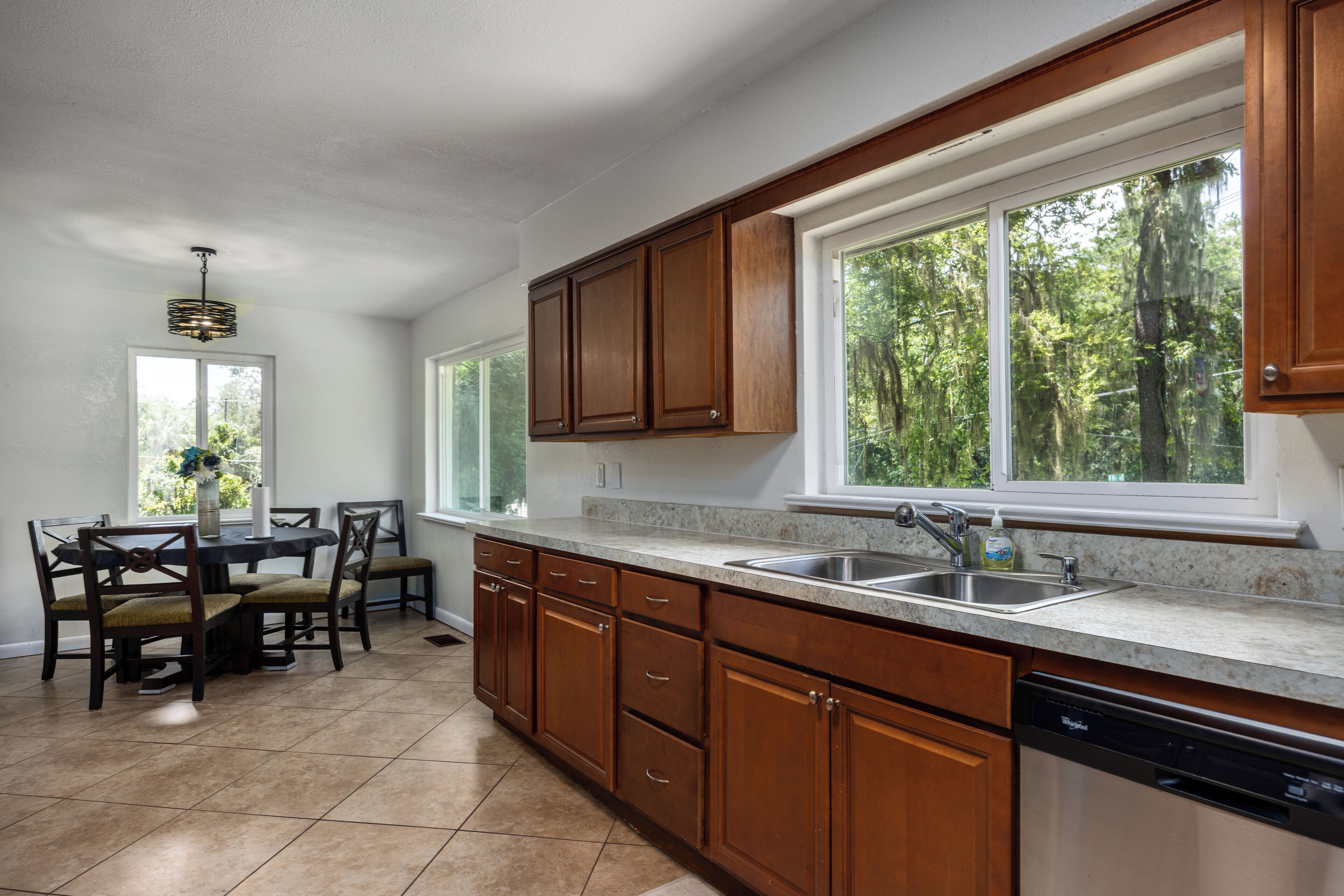 A kitchen with wooden cabinets, a granite countertop, a dishwasher, and a window with a view of trees.