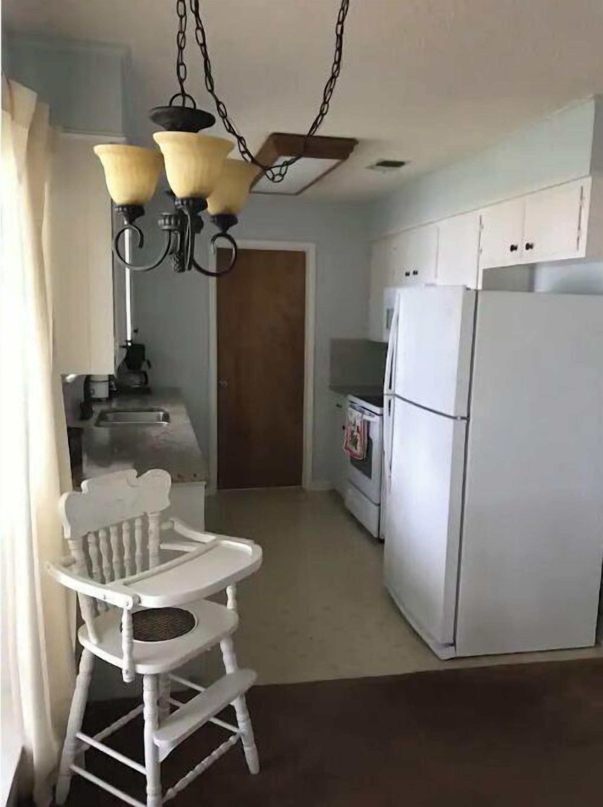 A kitchen with a white refrigerator, a white stove, and a white chair with a tray.
