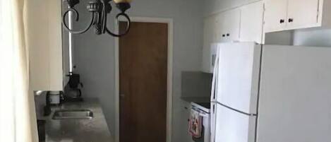 A kitchen with a white refrigerator, a white stove, and a white chair with a tray.