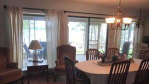 A dining area with a round table, chairs, a chandelier, and a view through large windows. - Lakehouse Getaway! (Pittsburg)