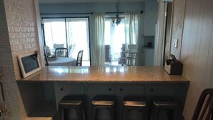 A kitchen with a granite countertop, four barstools, a chalkboard with a message, and a view of the dining area through a glass door. - Lakehouse Getaway! (Pittsburg)