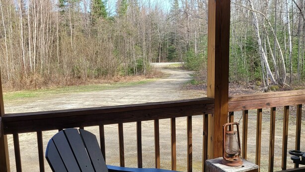 A wooden deck with a blue Adirondack chair, a lantern, and a view of a forested area. - White mountain getaway (Carroll)