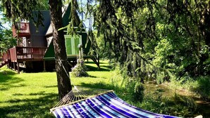 A hammock in a lush green outdoor setting with a wooden deck and a small building in the background. - Relaxing Scenic 1 Bedroom Retreat With Private Hot Tub (Findlay)