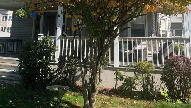 A two-story house with a porch and a tree in front. - Bright and cozy 3 bedroom apartment in Chicopee with AC, WiFi. Enjoy your stay (Chicopee)