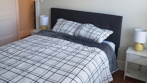 A neatly made bed with a checkered bedspread, two bedside lamps, and a closed door to the left. - Bright and cozy 3 bedroom apartment in Chicopee with AC, WiFi. Enjoy your stay (Chicopee)