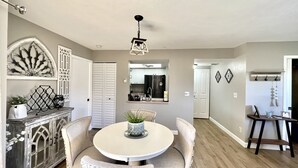 A dining area with a round table, two chairs, a decorative mirror, and a ceiling light fixture. - Newly updated 2br2br+Den golf course property near airport 90-day min stay (Fort Myers)