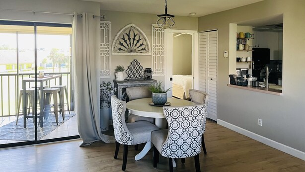 A dining area with a round table, two patterned chairs, a chandelier, and a view through a sliding glass door. - Newly updated 2br2br+Den golf course property near airport 90-day min stay (Fort Myers)