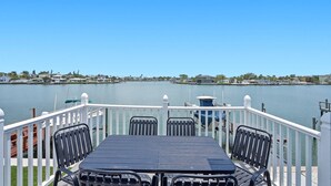 A deck with a table and chairs overlooking a body of water, with a railing and a clear view of the shoreline.