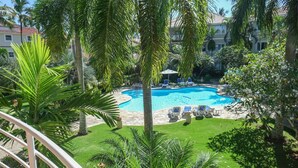 A swimming pool surrounded by palm trees and lounge chairs, with a view of a building in the background. - Nice 2 bedroom Apt. in Ocean Dream (Cabarete)