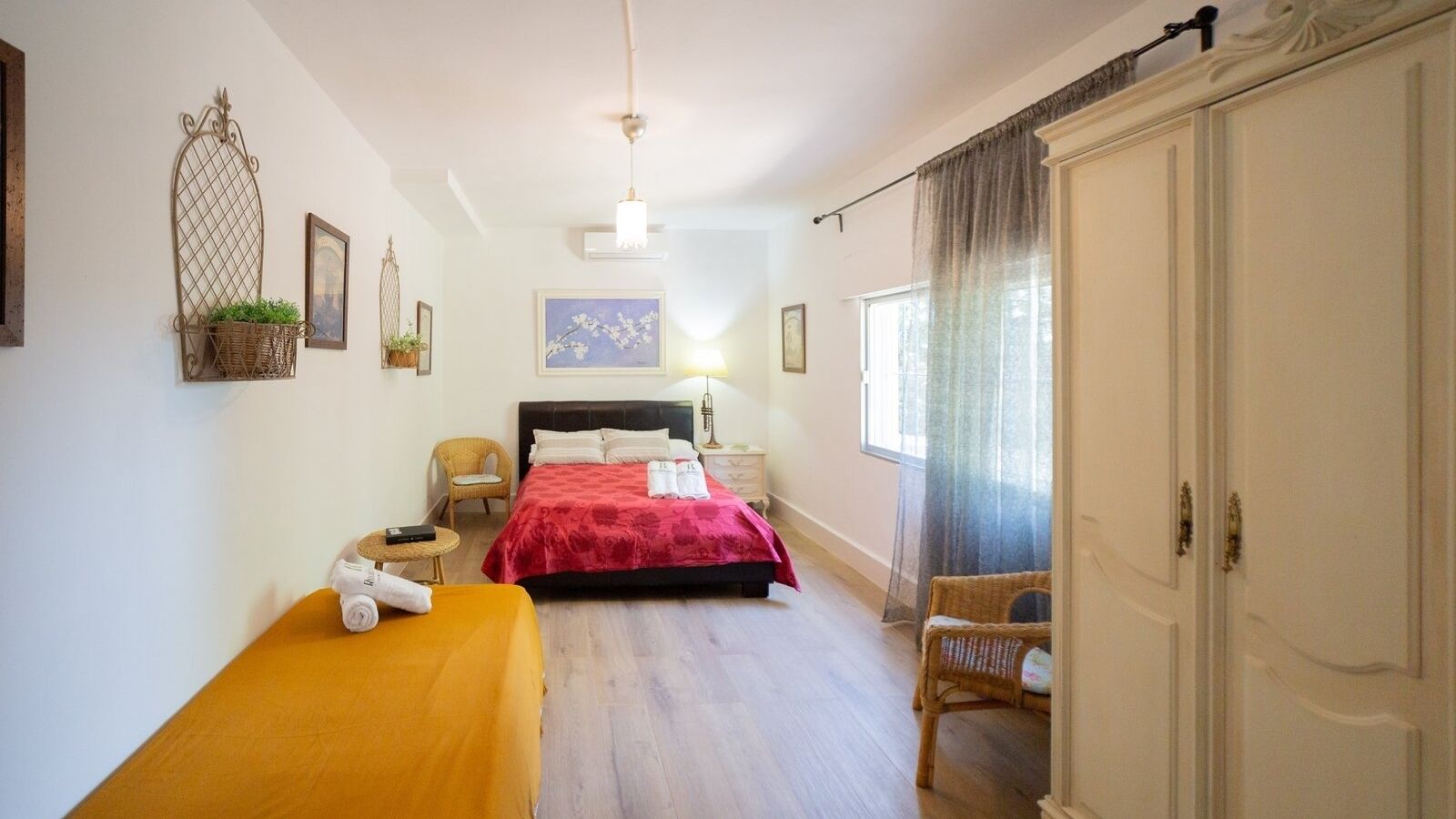 A hotel room with a bed, a small table with a chair, a wardrobe, and a window with curtains.