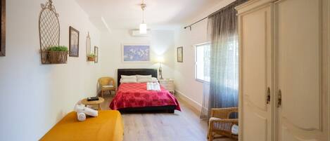 A hotel room with a bed, a small table with a chair, a wardrobe, and a window with curtains.