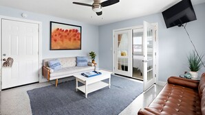 A living room with a white sofa, a coffee table, a ceiling fan, a TV mounted on the wall, and a sliding glass door leading to a balcony. - Waterfront condo overlooking the gorgeous intracoastal, Perfect for large family/group...sleeps up to 12 with 2 kitchens!  Well behaved dogs welcomed.  Bring your boat! (Indian Rocks Beach)