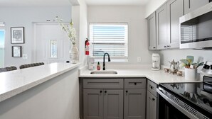A modern kitchen with a white countertop, grey cabinets, a stainless steel stove, and a window with blinds. - Waterfront condo overlooking the gorgeous intracoastal, Perfect for large family/group...sleeps up to 12 with 2 kitchens!  Well behaved dogs welcomed.  Bring your boat! (Indian Rocks Beach)