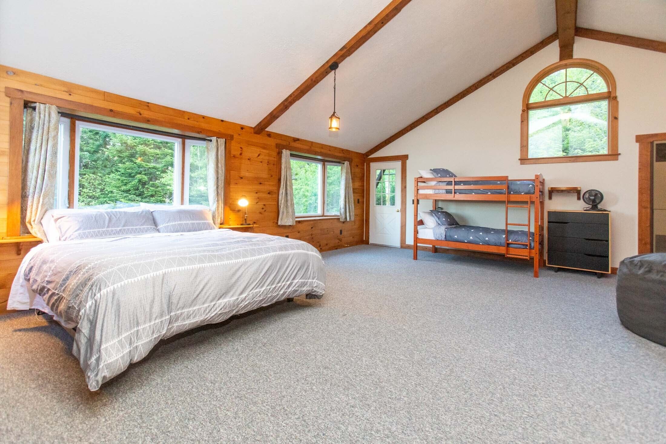 Une chambre avec un grand lit, un lit superposé, un bureau avec une chaise et une fenêtre avec des rideaux.