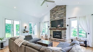 A spacious living room with a stone fireplace, large windows, and a modern sofa set. - Tranquil 4 bed 4 bath home in Collingwood (Collingwood)