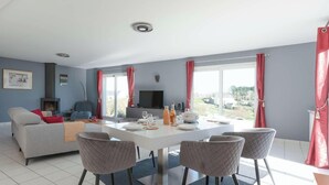 A modern living room with a sofa, TV, fireplace, dining area with chairs, and large windows. - Penn Ar Roz - Large house Pwd access near the sea (Saint-Pabu)