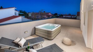 Eine Dachterrasse mit Whirlpool, Liegestühlen und einem Tisch mit Champagner.