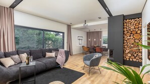 Ein modernes Wohnzimmer mit einem grauen Sofa, einem Essbereich mit Tisch und Stühlen und einem großen Fenster mit Vorhängen.