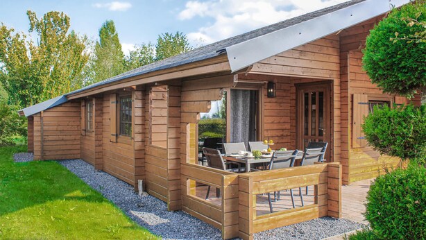 Una cabaña de madera con un patio, que incluye una mesa y sillas, rodeada de follaje.