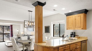 A modern kitchen with wooden cabinets, a granite countertop, and a dining area with a table and chairs. - Shadow Ridge 400 | Walk to Lifts | Mtn Views | Kitchen | Fireplace | Top Floor | Pool & Hot Tub (Park City)