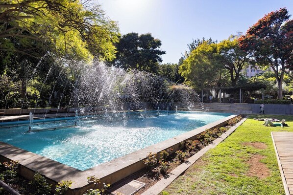 A rectangular pool with multiple water jets, surrounded by a grassy area and trees.