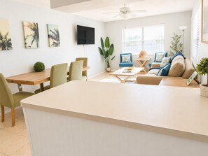 A modern living room with a dining area, a flat-screen TV mounted on the wall, and a ceiling fan.