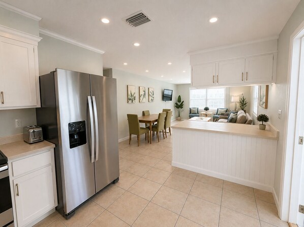 A modern kitchen with a stainless steel refrigerator, a dining area with a table and chairs, and a small island with a sink.