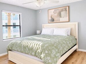 A bedroom with a bed, a ceiling fan, a window with blinds, and a painting on the wall.