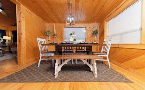 A wooden dining room with a table and chairs, a chandelier, and potted plants.