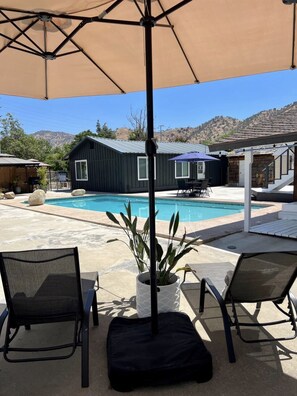 A poolside area with two lounge chairs, a table, and a large umbrella.