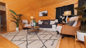 Un salon chaleureux, décoré avec des meubles en bois, comprenant un canapé, un fauteuil et une table basse, agrémenté d’une grande plante et d’un tableau encadré au mur.