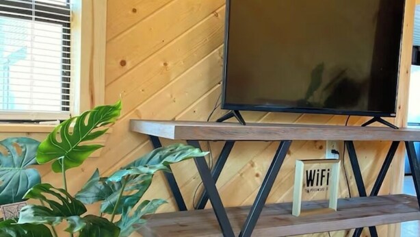 Un intérieur en bois avec un téléviseur posé sur un support métallique, un panneau indiquant la présence d’une connexion Wi-Fi et une enseigne « Résidence au bord du lac ».