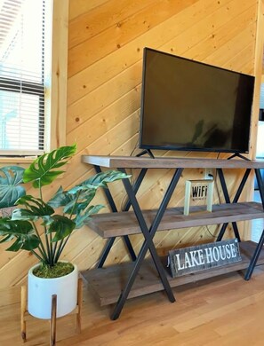 Puinen sisustus, jossa on metallijalalla varustettu televisio, Wi-Fi-symboli ja kyltti, jossa lukee ”Lake House”.